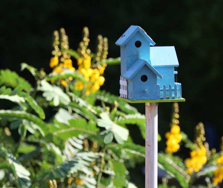 Blue birdhouse on a white pole with yellow flowers in the background